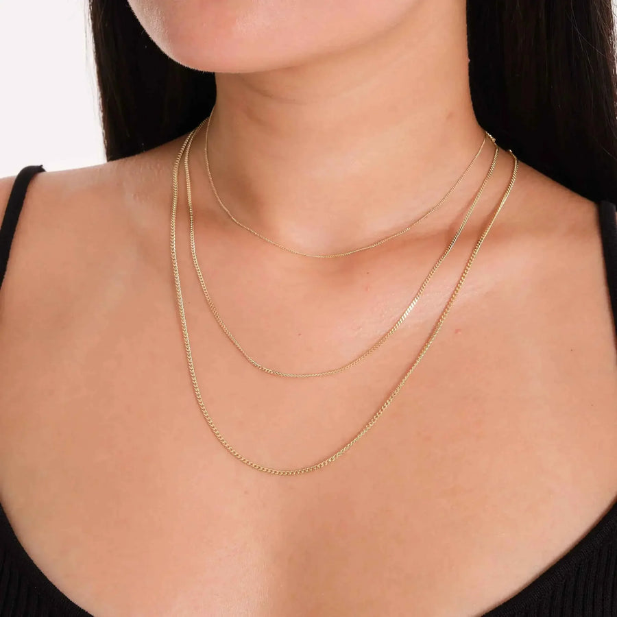 Gros plan de chaînes gourmette plate en or jaune 14 carats superposées au cou