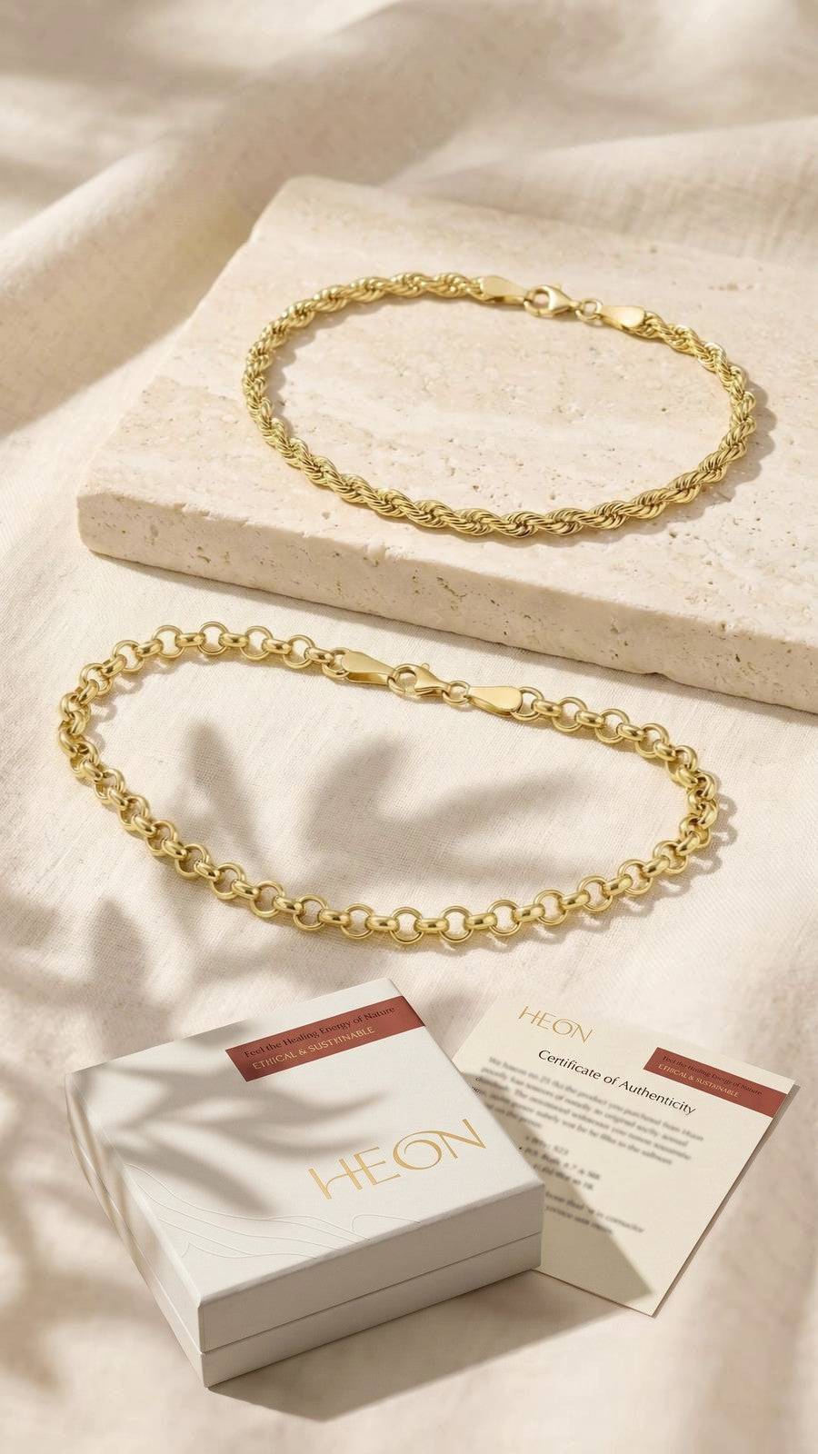 L'écrin blanc HEON et son certificat d'authenticité sur du lin, sous un bracelet maille corde et un bracelet maille rolo en or 14 carats