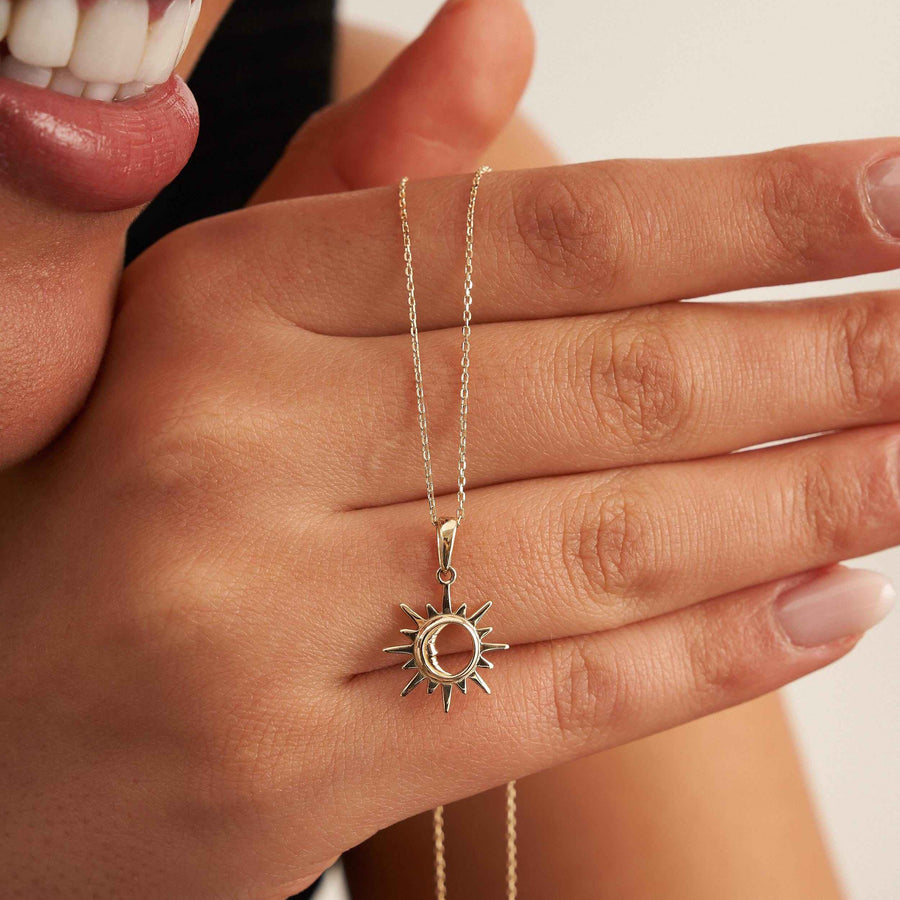 Primo piano della mano della modella che tiene una collana con ciondolo sole e luna in oro 14kt