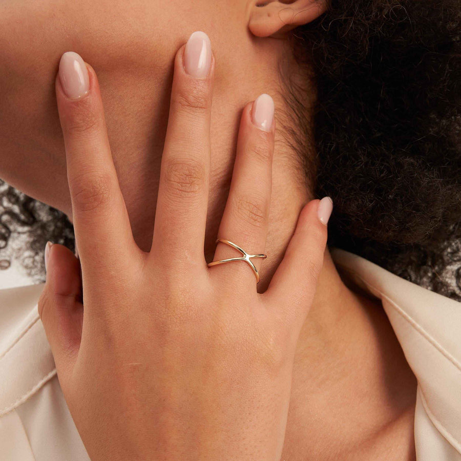 Bague infini entrecroisée en or 14 carats portée sur une main posée contre le cou