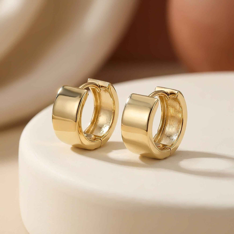Coppia di orecchini huggie spessi in oro giallo 14kt su un piedistallo color crema