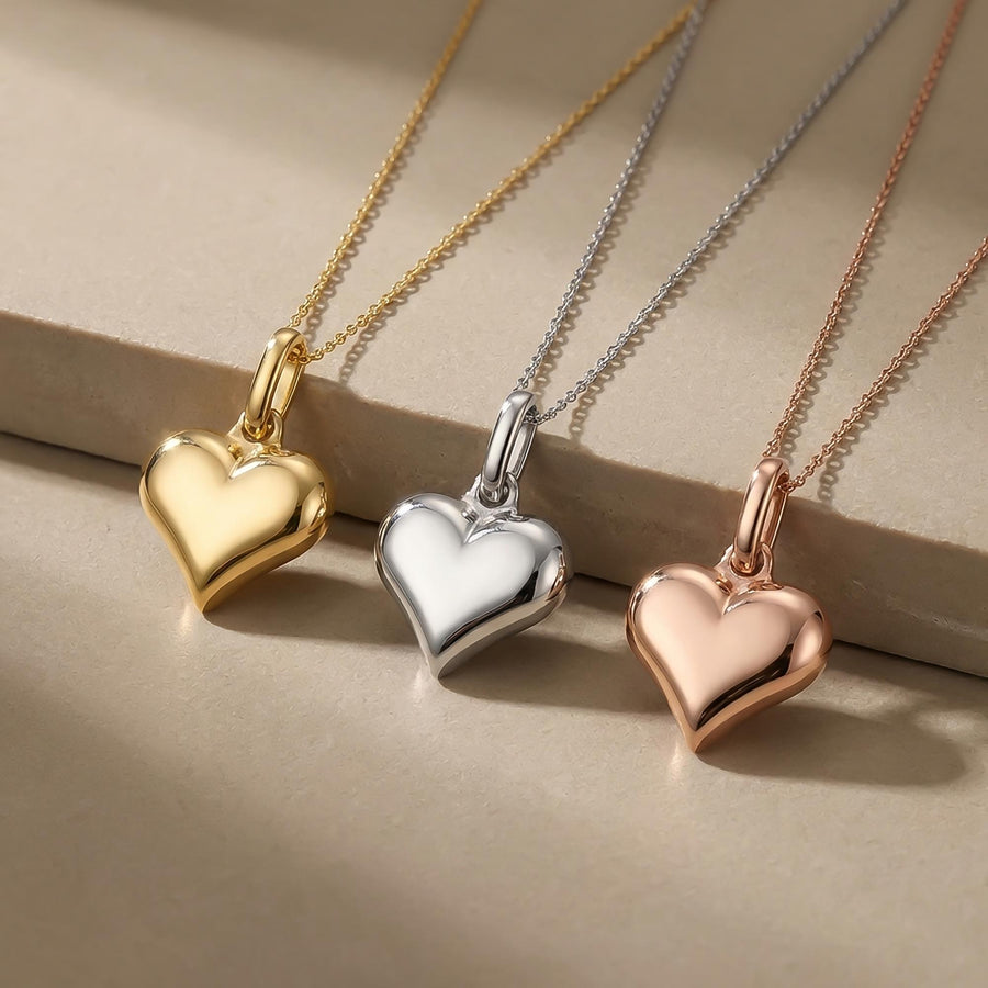 Close-up of 14K yellow, white and rose gold puffed heart pendants on a stone ledge