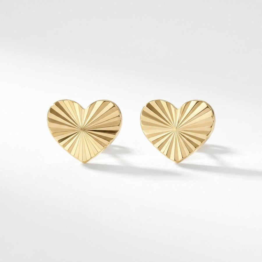 Pair of 14K yellow gold diamond-cut heart stud earrings on a soft grey background