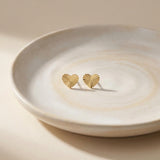 14K yellow gold diamond-cut heart stud earrings on a ceramic dish