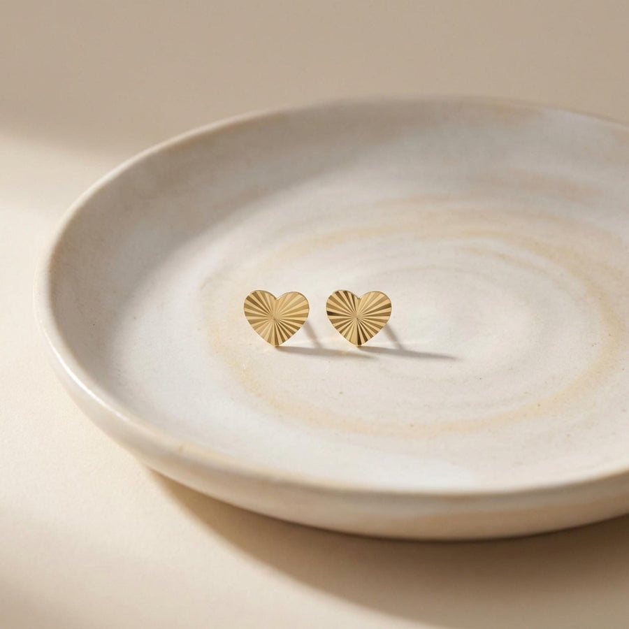 14K yellow gold diamond-cut heart stud earrings on a ceramic dish
