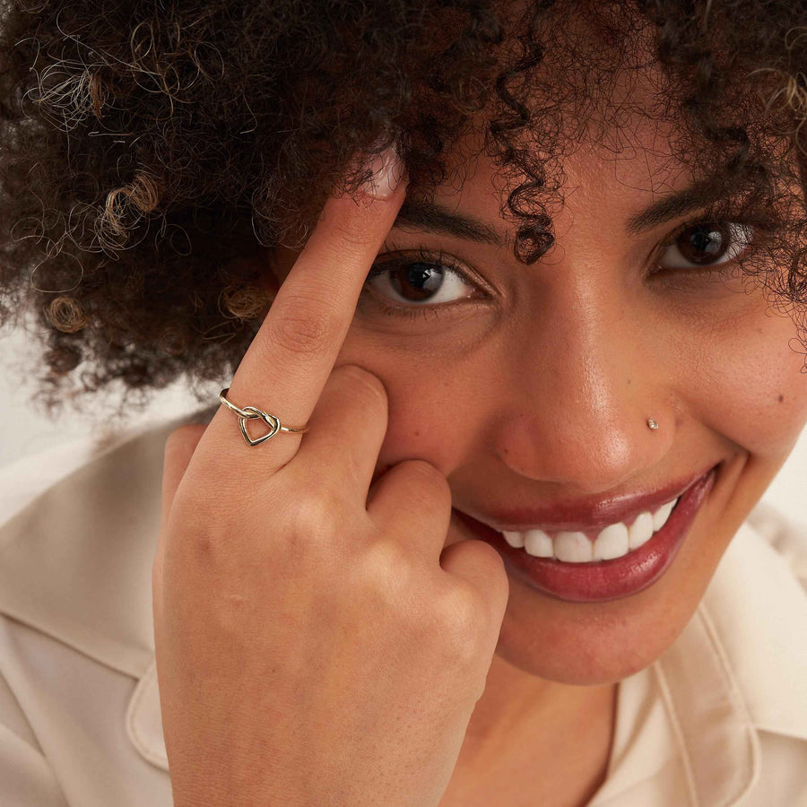 Modella sorridente si tocca vicino all'occhio e indossa un anello aperto con cuore infinito in oro 14kt