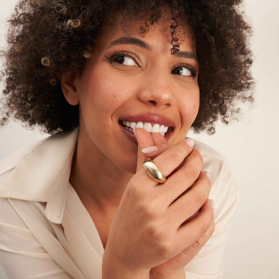 Anillo cúpula ancho en oro amarillo de 14 quilates en la mano de la modelo, alzada hacia sus labios sonrientes