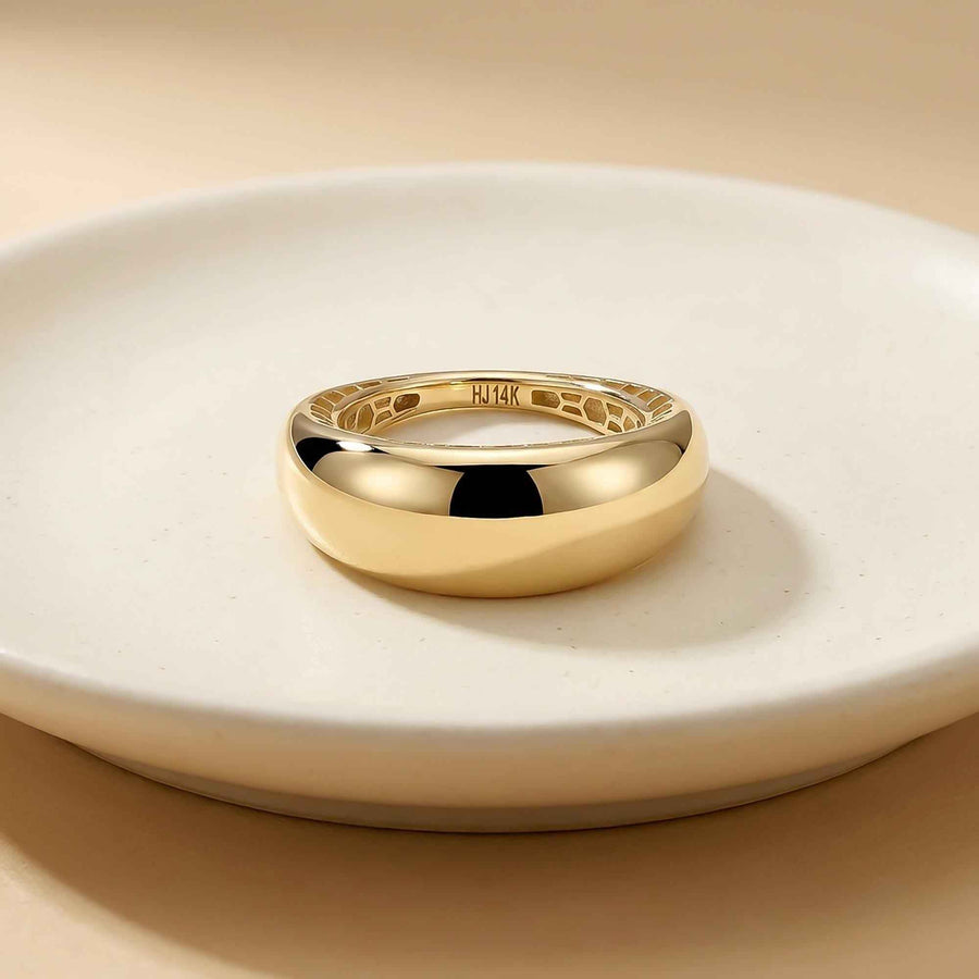 Anillo cúpula ancho en oro amarillo de 14 quilates en vertical sobre un plato de cerámica blanco