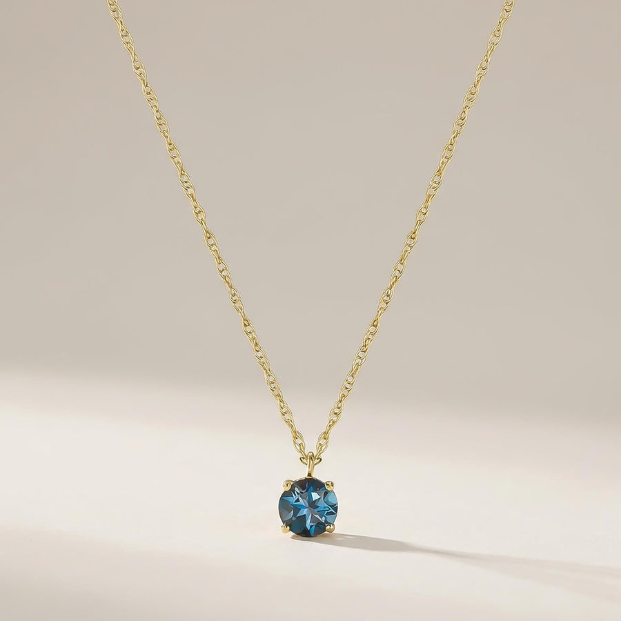 London-Blue-Topas-Solitärhalskette aus 585er Gelbgold vor cremefarbenem Hintergrund in weichem Licht