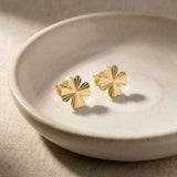 Pendientes de botón de trébol diamantados en oro amarillo de 14 quilates en un plato de cerámica