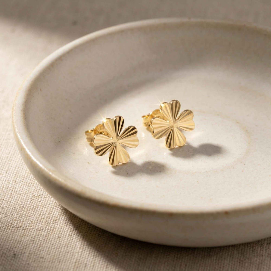 Pendientes de botón de trébol diamantados en oro amarillo de 14 quilates en un plato de cerámica
