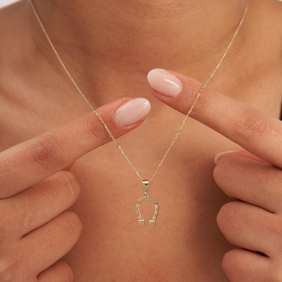 Doigts tenant le pendentif fer à cheval en or jaune 14 carats au cou