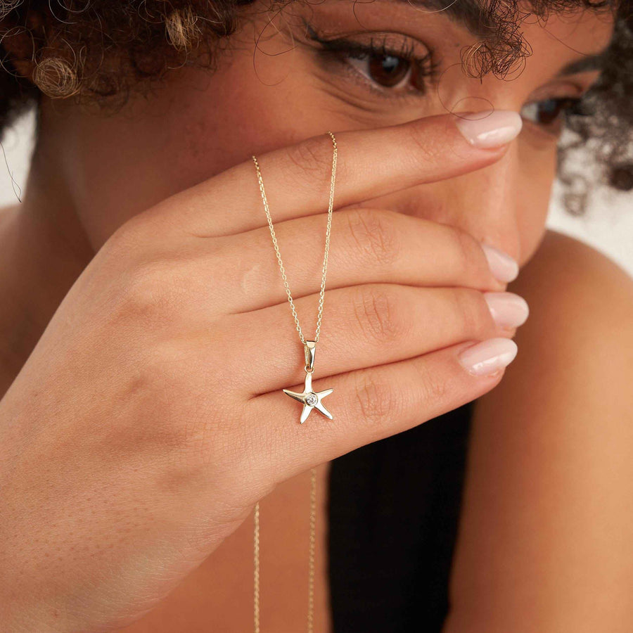 Mannequin se cachant le visage d'une main, portant un collier pendentif étoile de mer en or 14 carats