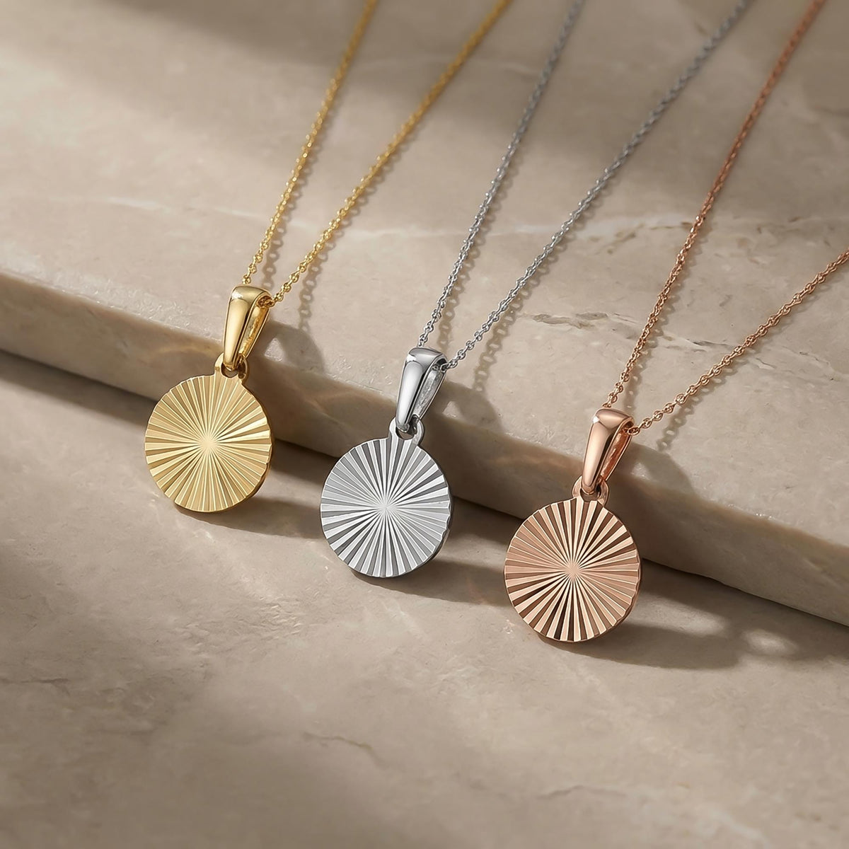 Collares de disco de sol radiante en oro amarillo, blanco y rosa de 14 quilates sobre una repisa de piedra
