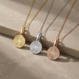 Collares de disco de sol radiante en oro amarillo, blanco y rosa de 14 quilates sobre una repisa de piedra
