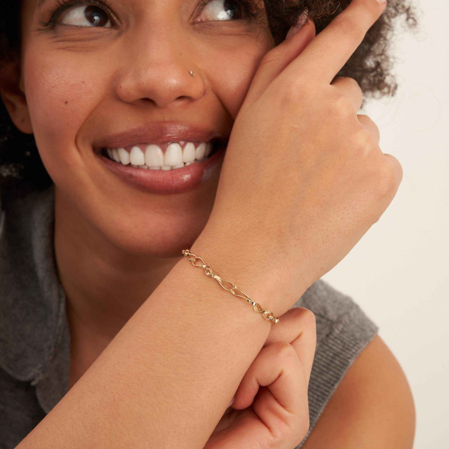 Modelo sonriente con la muñeca alzada para mostrar una pulsera de cadena retorcida de eslabones infinito en oro amarillo de 14 quilates