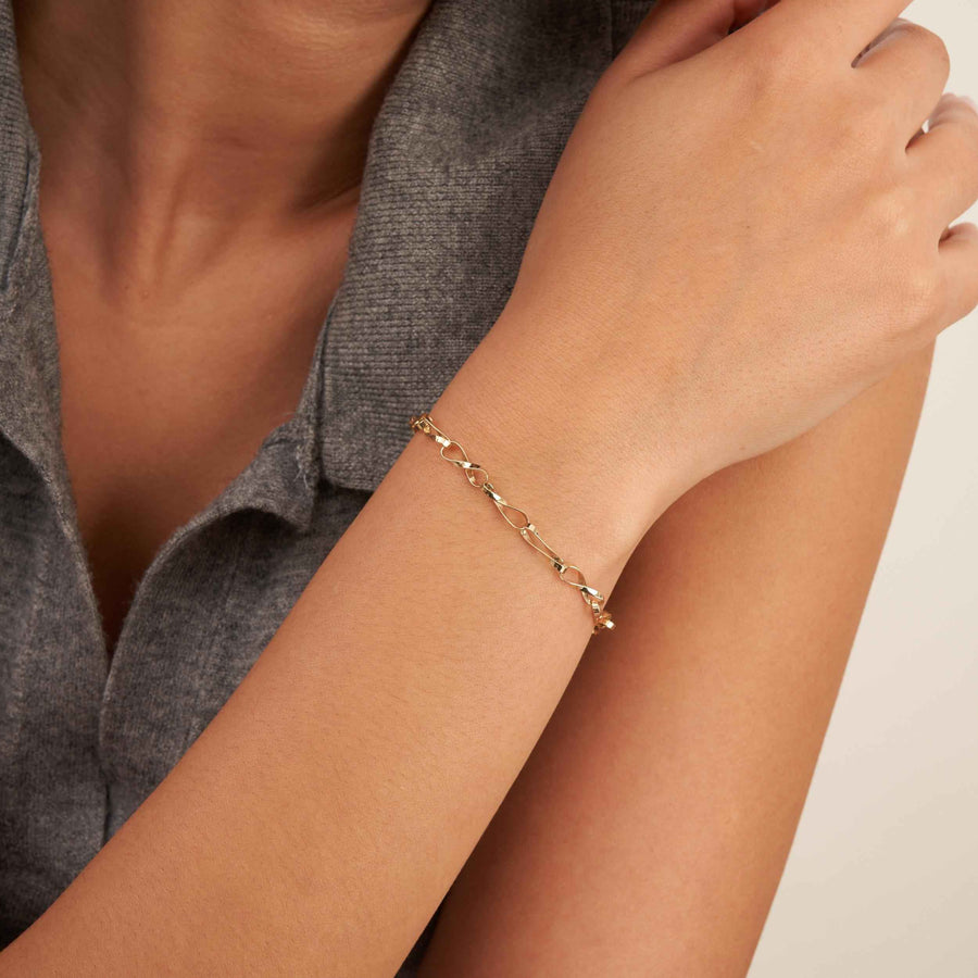 Pulsera de cadena retorcida de eslabones infinito en oro amarillo de 14 quilates puesta, con la mano apoyada en el hombro