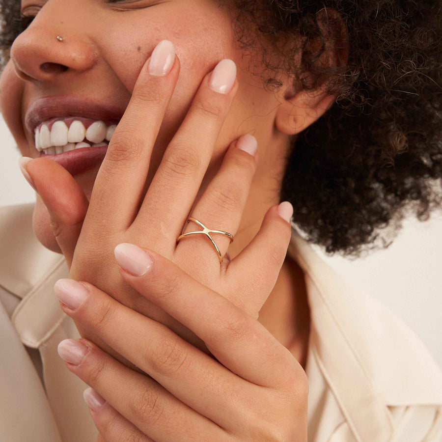 Mannequin souriant, main sur la joue, portant une bague infini entrecroisée en or 14 carats