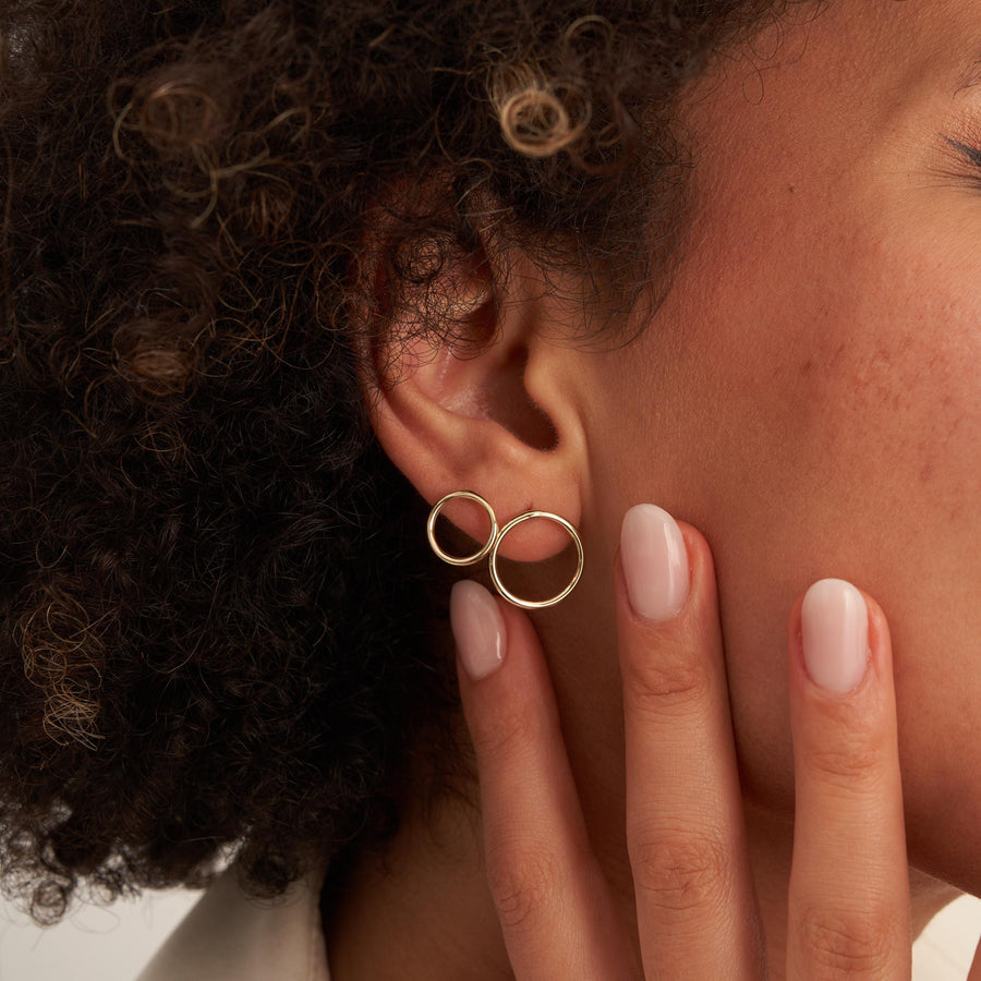 Gros plan sur une oreille avec deux puces d'oreilles cercle en or jaune 14 carats portées, la main à la mâchoire