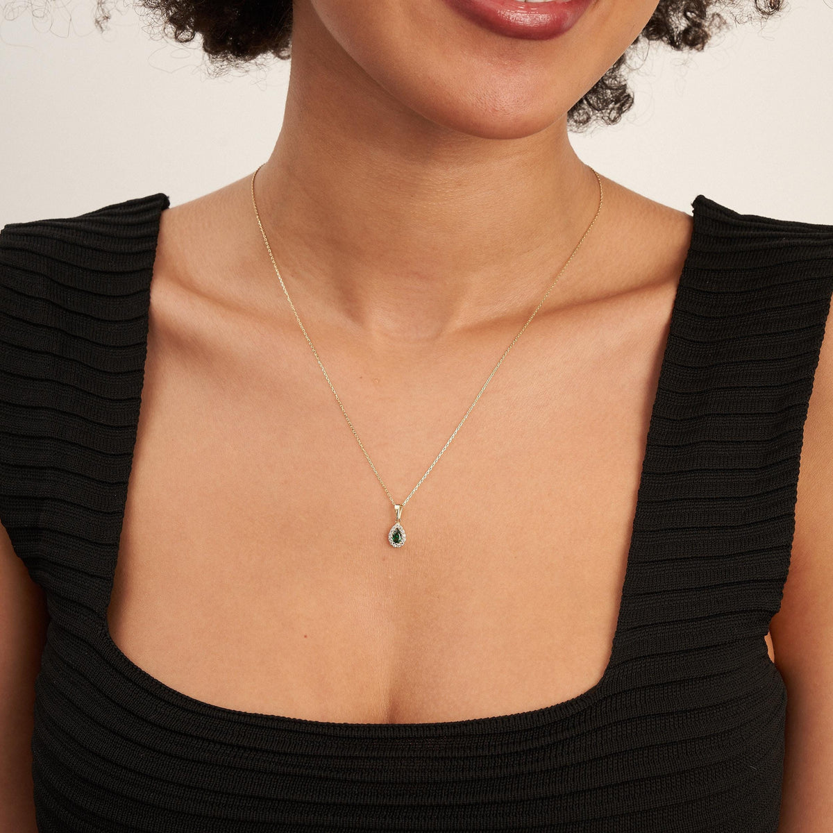 Modella sorridente con top nero indossa una collana in oro giallo 14kt con smeraldo taglio pera creato in laboratorio