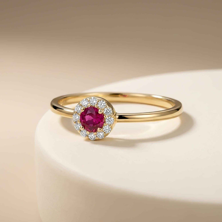 Bague fine halo rubis de synthèse en or jaune 14 carats présentée sur un socle crème