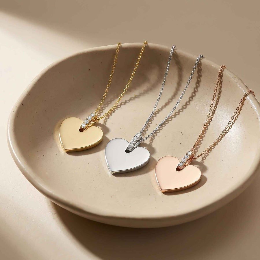 Collares de corazón grabado personalizados en oro amarillo, blanco y rosa de 14 quilates en un cuenco de cerámica beige