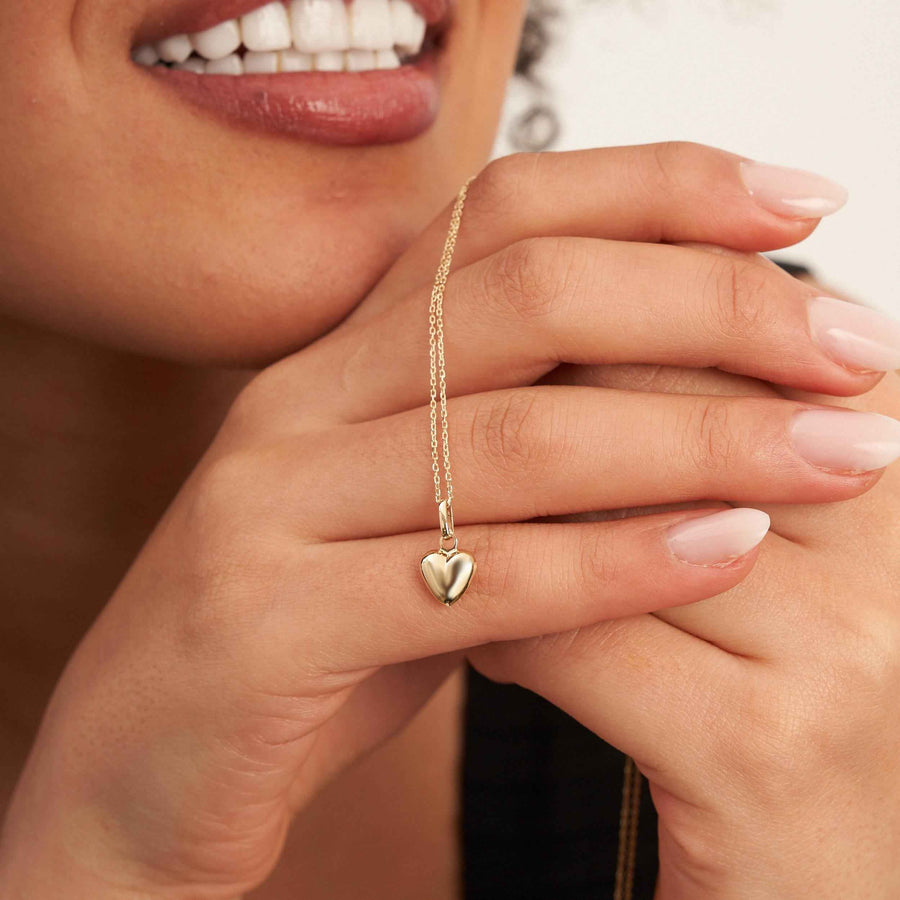 Collier cœur bombé 3D en or jaune 14 carats tenu entre les doigts du mannequin près du menton