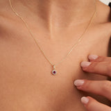 Pendentif halo rubis rond de synthèse en or jaune 14 carats posé sur la poitrine, main à proximité