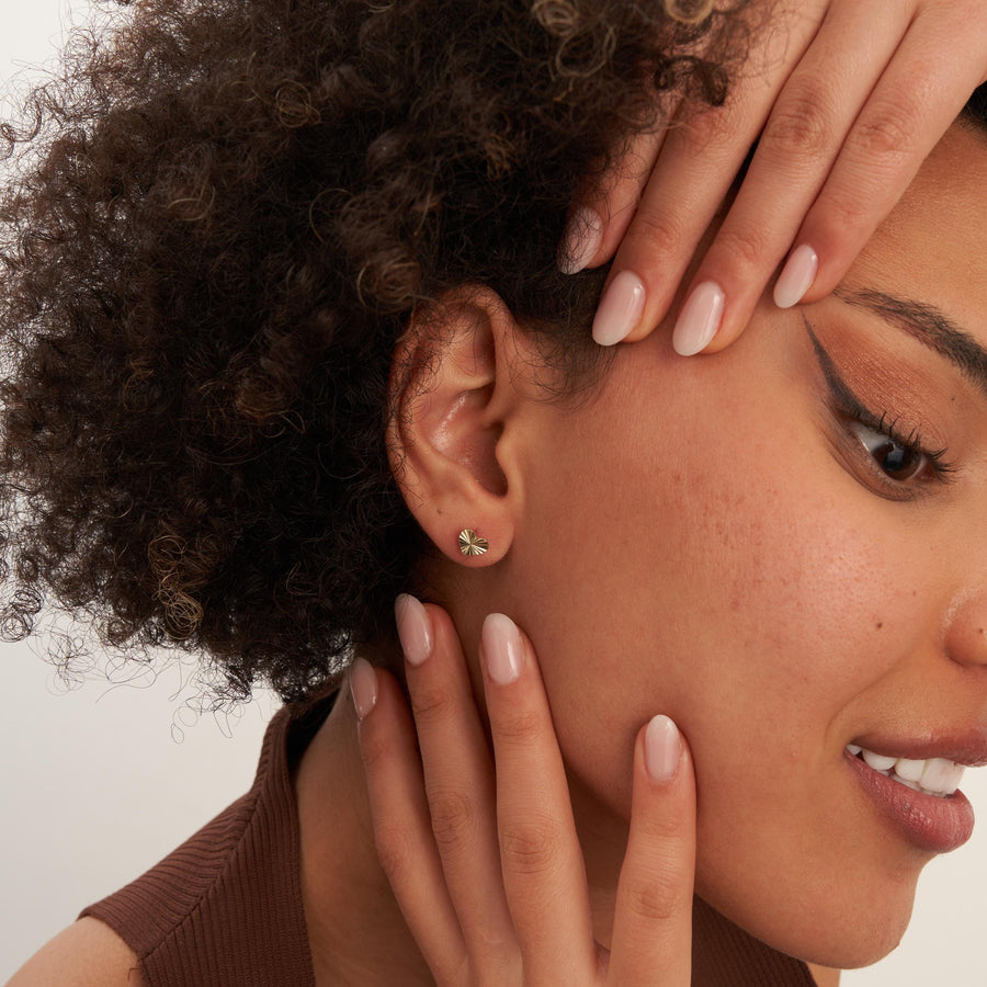 Model with hand in her hair wearing 14K yellow gold diamond-cut heart stud earrings