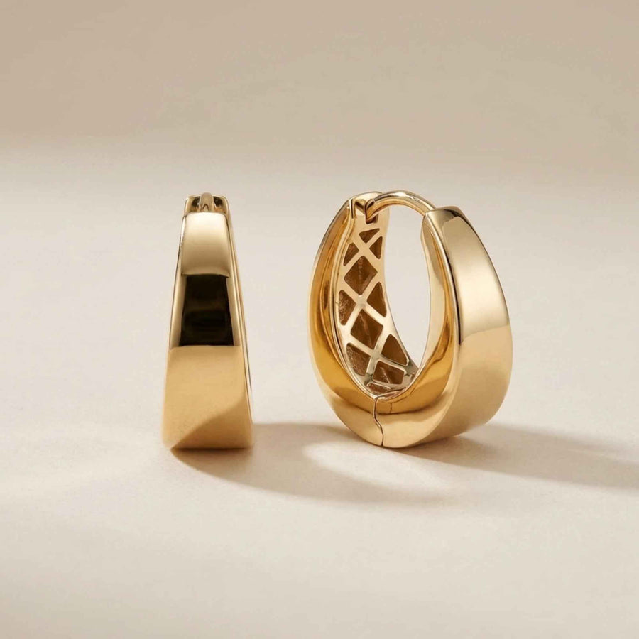 Par de pendientes de aro gruesos con bisagra en oro amarillo de 14 quilates en vertical sobre fondo crema