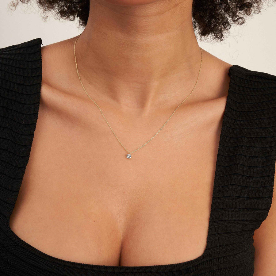 Collier solitaire topaze blanche en or 14 carats porté sur le décolleté avec un haut noir, vue de face