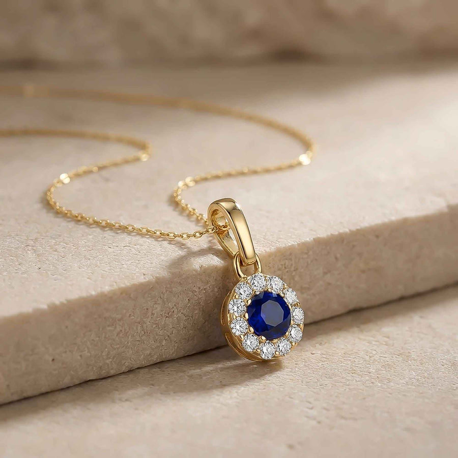 Gros plan du pendentif halo saphir rond de synthèse en or jaune 14 carats sur un bloc de pierre