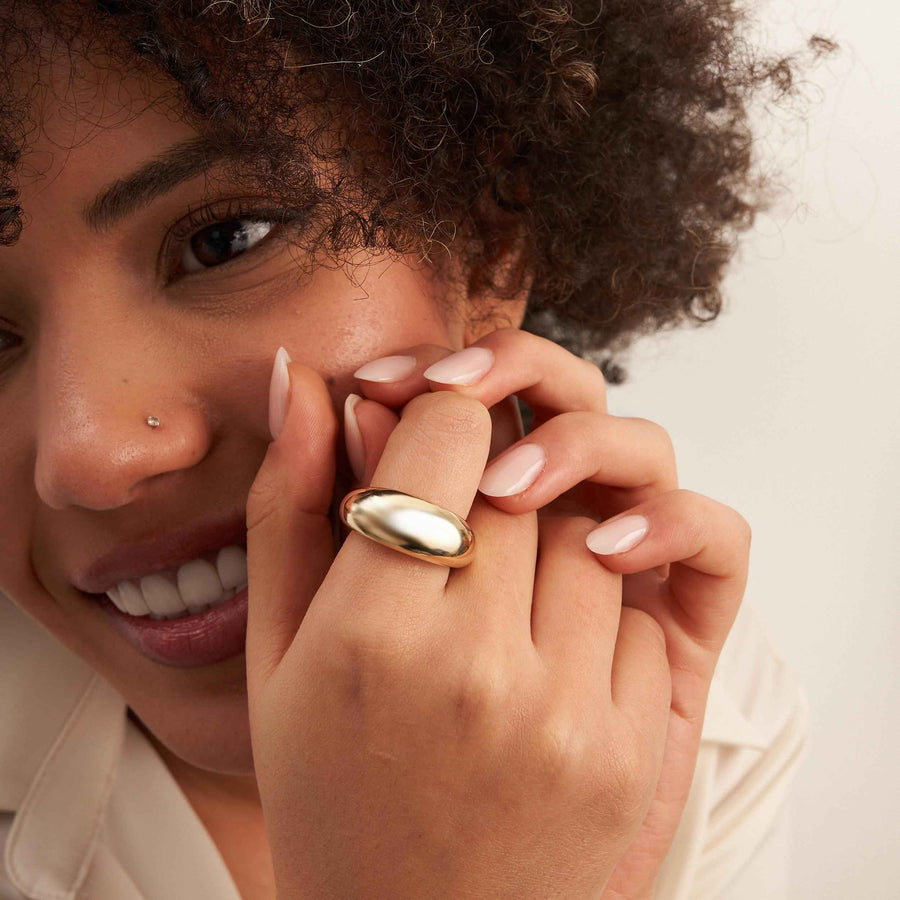 Primer plano del anillo cúpula ancho en oro amarillo de 14 quilates en el dedo; la modelo sonríe a cámara