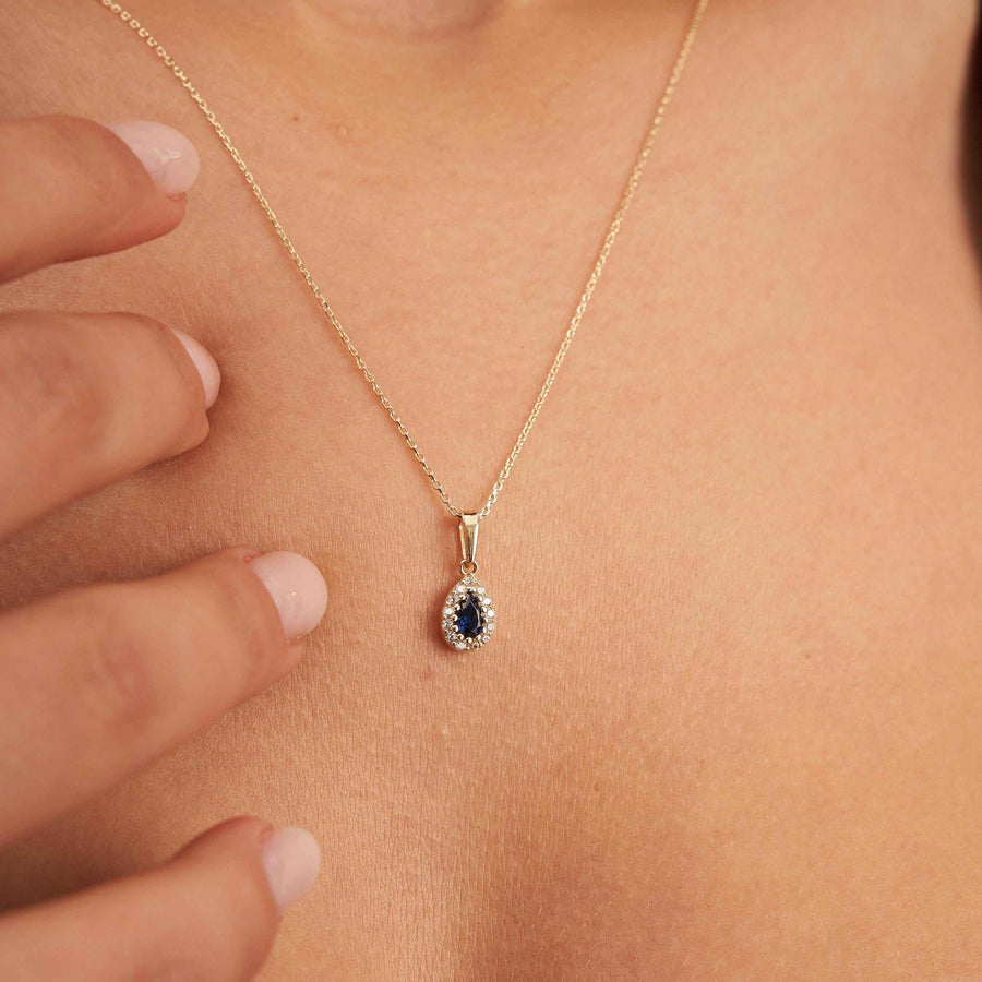 Collier pendentif halo saphir poire de synthèse en or 14 carats au cou, bout des doigts sur la clavicule