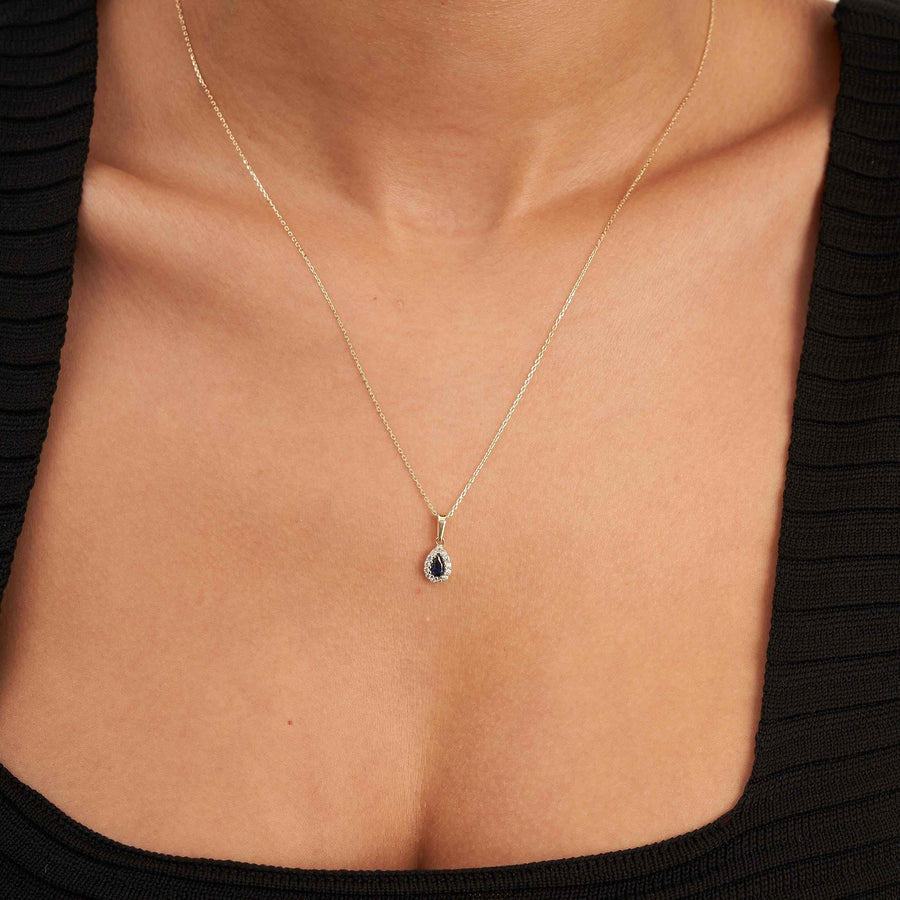Gros plan du collier pendentif halo saphir poire de synthèse en or jaune 14 carats porté au cou