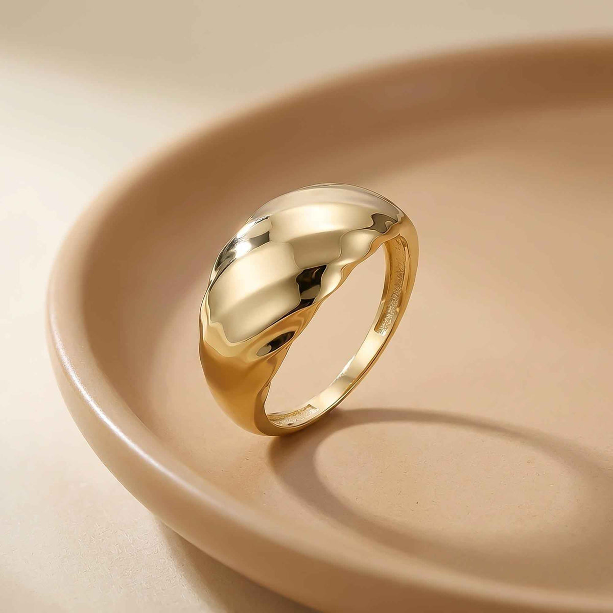 Swirl-Kuppelring aus 585er Gelbgold in einer Keramikschale auf Beige