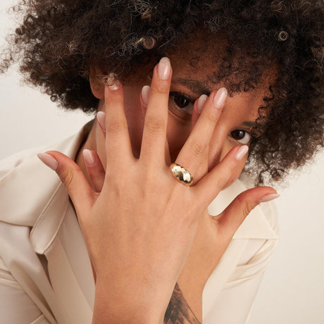 Anillo cúpula espiral en oro amarillo de 14 quilates en la mano de la modelo, apoyada sobre su rostro