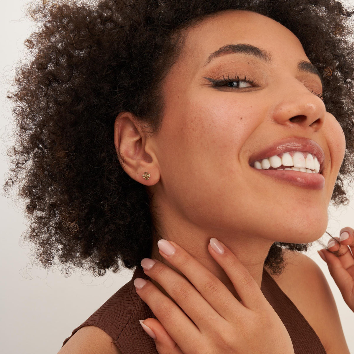 Pendientes de botón de trébol en oro amarillo de 14 quilates llevados por la modelo sonriente, con la mano en el cuello