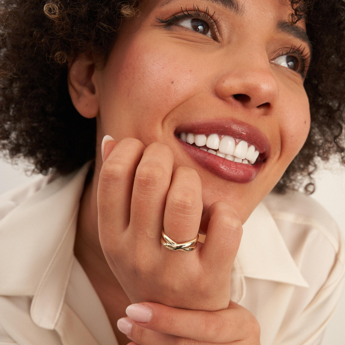 Modelo sonriente con la barbilla apoyada en la mano y un anillo cruzado en oro amarillo de 14 quilates