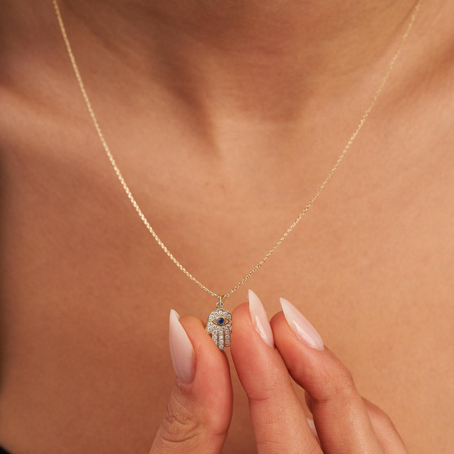 Punta delle dita che tiene una collana mano di Fatima in oro giallo 14kt con zaffiro blu creato in laboratorio