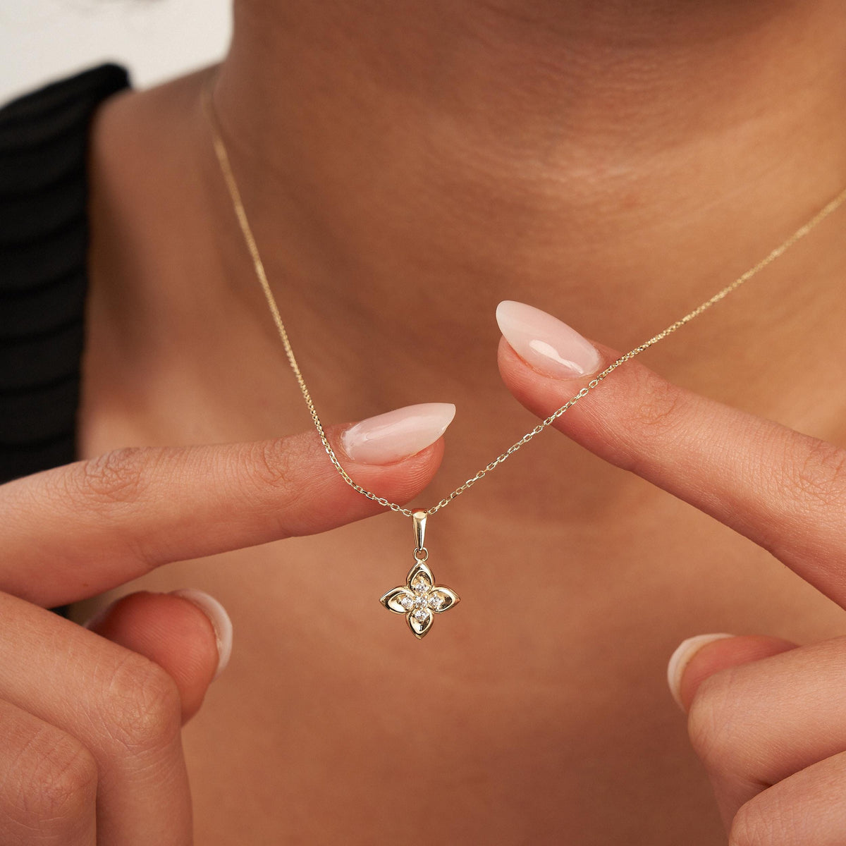 Doigts tenant le pendentif fleur trèfle en or jaune 14 carats à l'encolure
