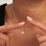 Doigts tenant le pendentif fleur trèfle en or jaune 14 carats à l'encolure