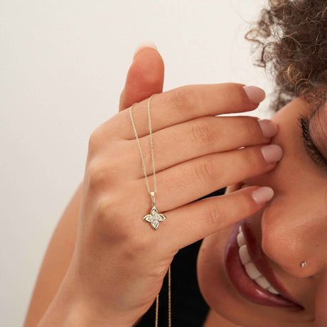 Mannequin souriant tenant la chaîne d'un collier fleur trèfle en or jaune 14 carats