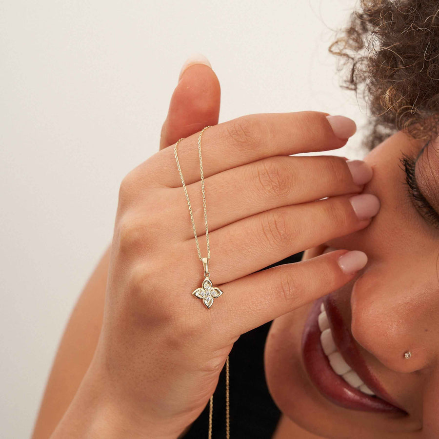 Mannequin souriant tenant la chaîne d'un collier fleur trèfle en or jaune 14 carats