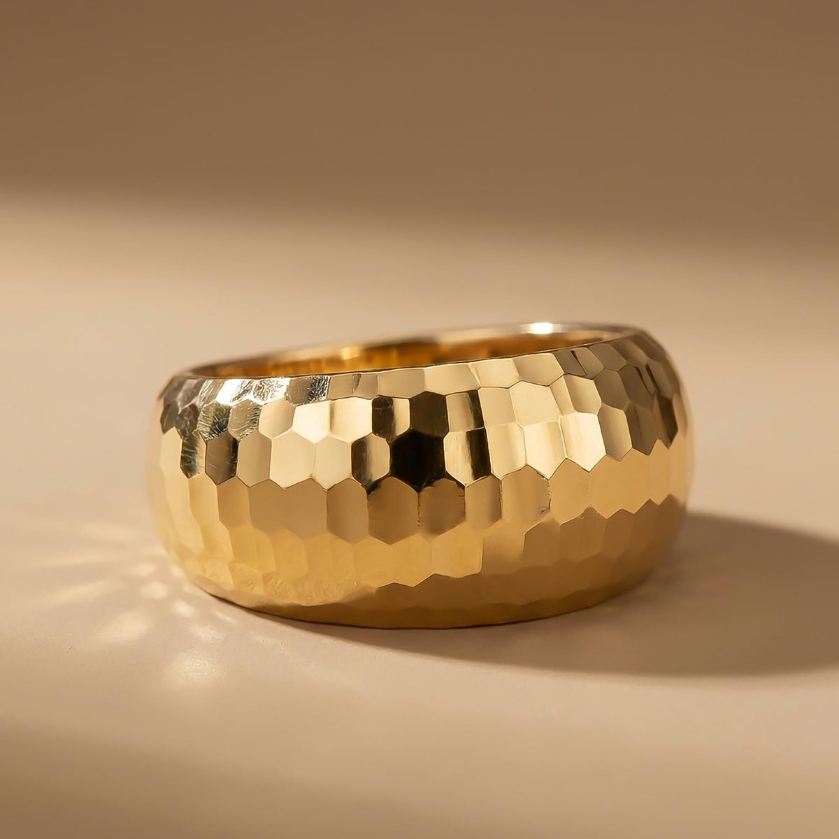 Facettierter, diamantierter Kuppelring aus 585er Gelbgold vor beigem Hintergrund
