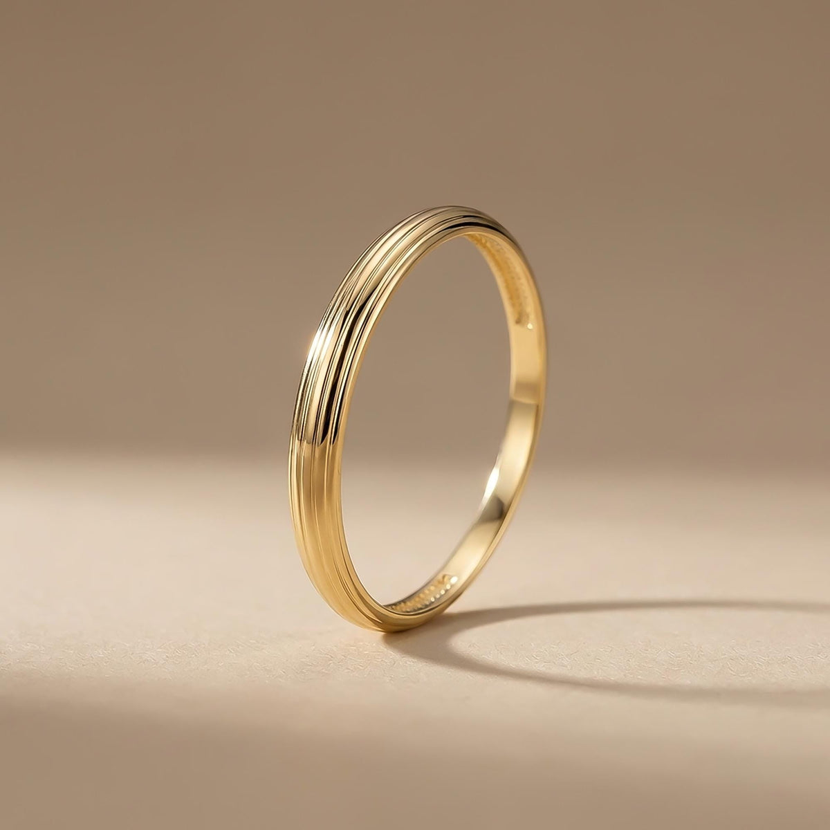 Anillo acanalado en oro amarillo de 14 quilates en vertical sobre fondo beige