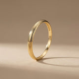 Anillo acanalado en oro amarillo de 14 quilates en vertical sobre fondo beige