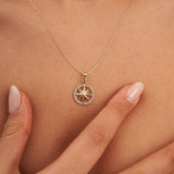 Fingers holding the 14K yellow gold compass star pendant at the neckline