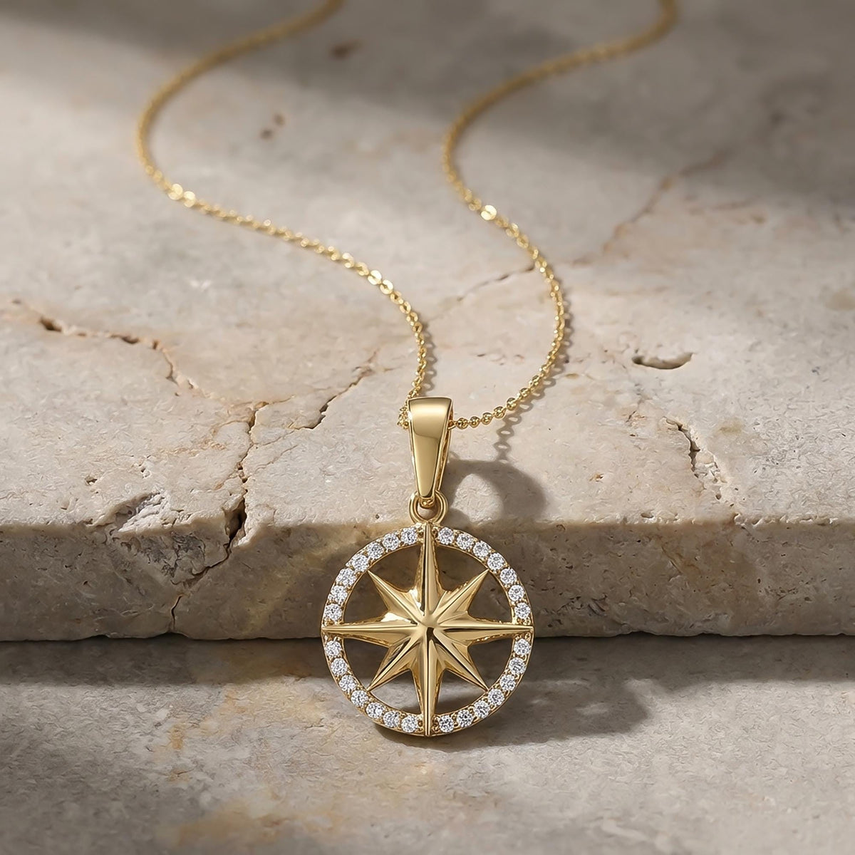 Close-up of 14K yellow gold compass star pendant on textured stone