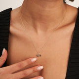 Close-up of 14K yellow gold infinity necklace worn with hand on the chest